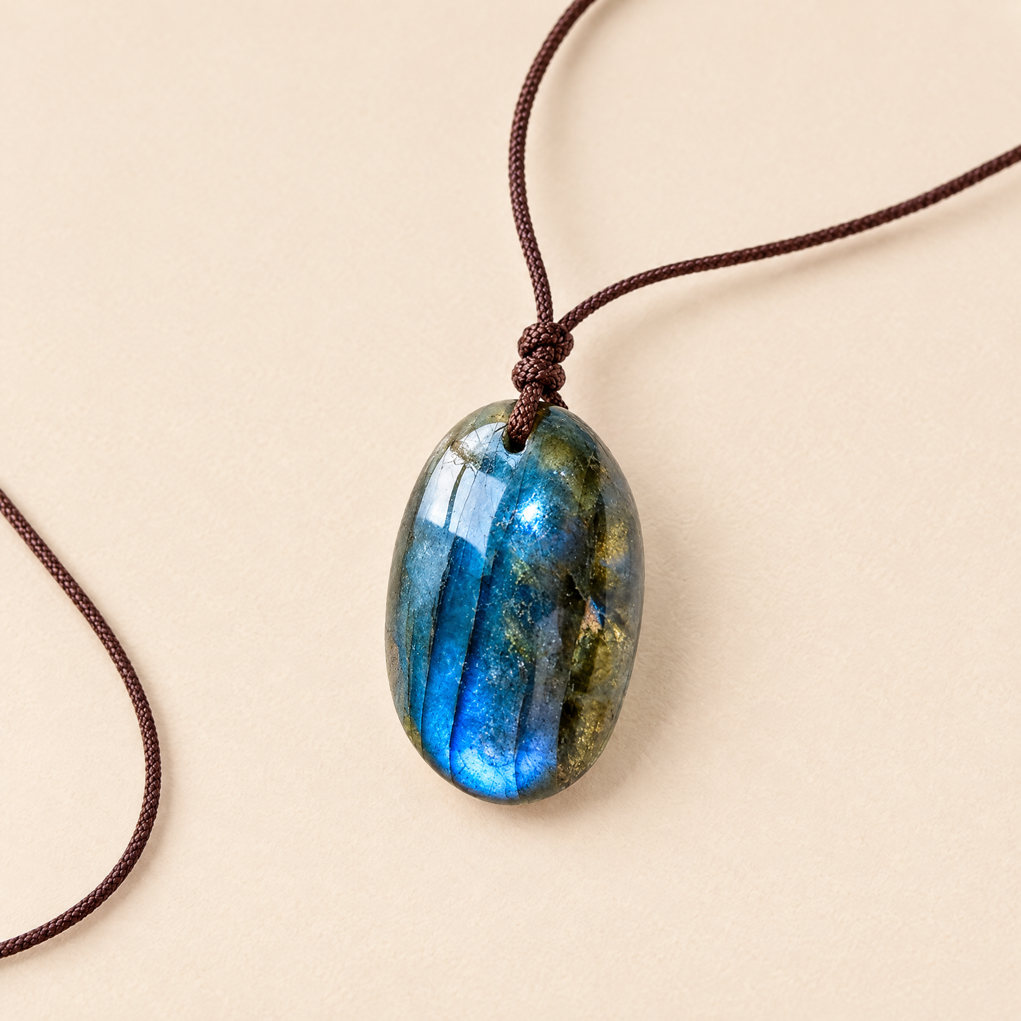 Intuition pendant: smooth labradorite stone with blue flash on a brown cord, cream background